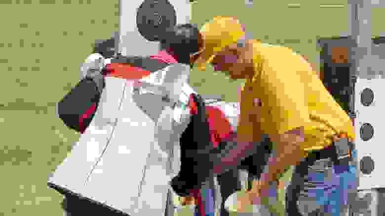 Man in a Yellow Shirt and Cap helping a Competitor with their Target