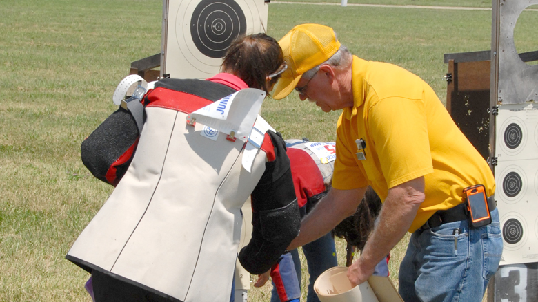 Coach Helps a Competitor with their Paper Target on an Outdoor Range